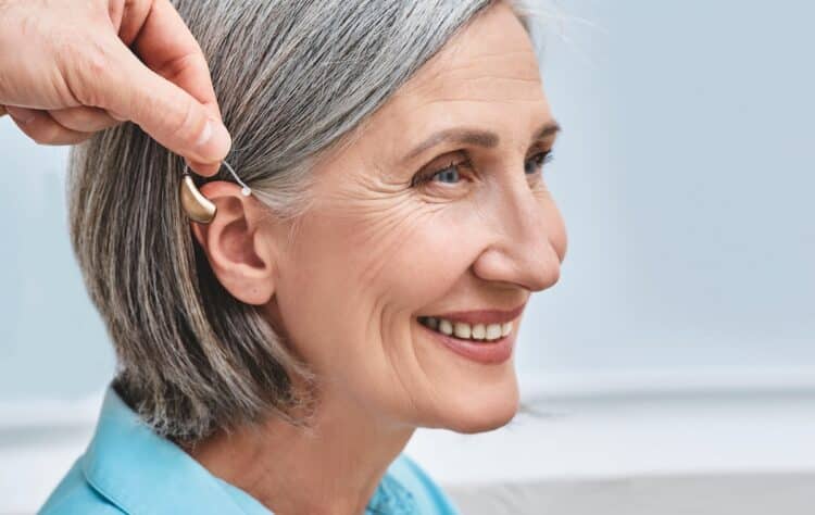 Close-up of hearing aid near senior female patient's ear at audiology clinic. Hearing solutions, hearing BTE aids